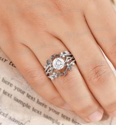 a woman's hand with a diamond ring on top of her finger and an old book in the background