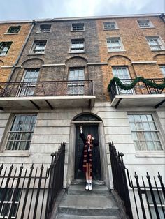 a woman is standing in the doorway of a large brick building with black iron railings