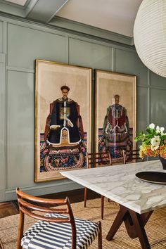 two paintings hang on the wall above a dining room table with chairs and a vase filled with flowers