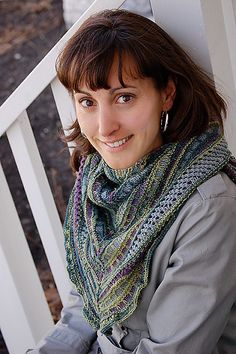 a woman sitting on a white bench wearing a knitted scarf and smiling at the camera