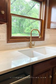 a kitchen sink under a window in front of a wooden cabinet and countertop with white tile