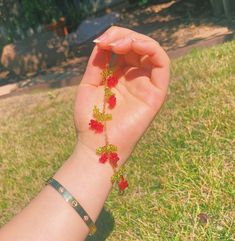 a woman's hand holding onto a bracelet with red flowers on it and green grass in the background