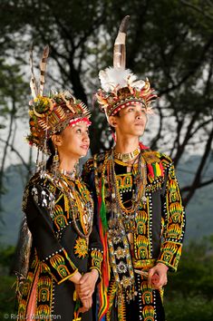 two people dressed in colorful clothing standing next to each other with feathers on their head