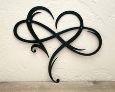 a metal heart with an intricate design on the side of a white wall next to a wooden table