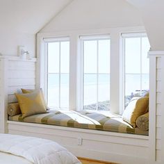 a bedroom with white walls and wooden floors has a large window seat on the bed