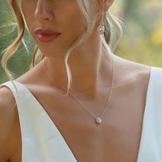 a woman with blonde hair wearing a white dress and diamond pendants on her neck