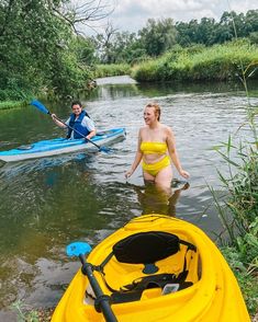 two people in yellow swimsuits paddling kayaks on a river with grass and trees