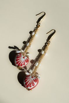 pair of red and white heart shaped earrings with dangling pearls on black earwires