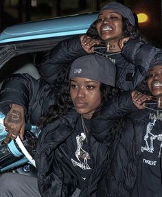 three women in black jackets and hats sitting on the back of a car