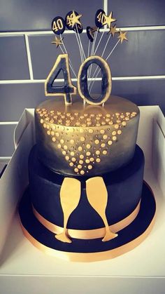 a black and gold cake with two champagne glasses on top is sitting in a box