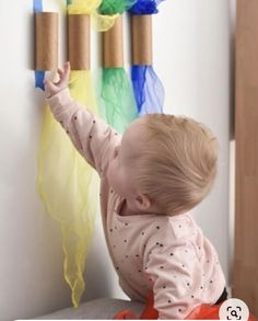 a baby playing with some toilet paper on the wall in front of it's colorful streamers