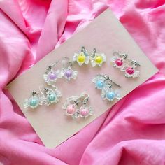 six pairs of earrings are laying on a pink cloth next to a piece of paper