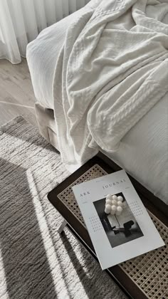 an open magazine sitting on top of a bed next to a white comforter and pillows