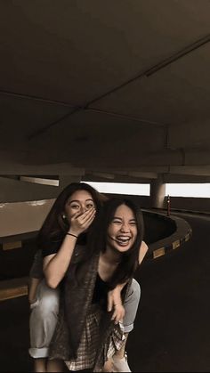 two young women are posing for the camera in an empty parking garage with their arms around each other