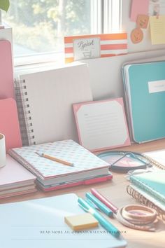 an office desk with notebooks, pens and coffee cup on it in front of a window