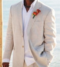 a man in a white suit and flower boutonniere standing by the water