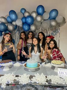 a group of women standing in front of a table with cake and balloons on it