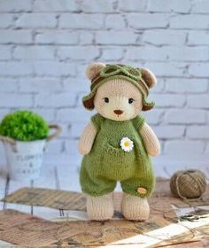 a small teddy bear with a green outfit and flower in its hand on a table next to a ball of yarn