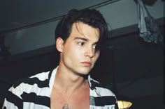 a man with a tattoo on his chest looking at the camera while wearing a striped shirt