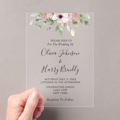 a person holding up a wedding card with flowers on the front and bottom, in front of a gray background