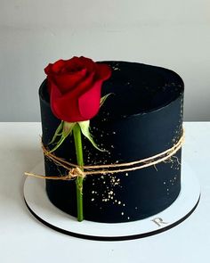 a black cake with a single red rose on top and gold sprinkles