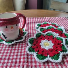 two crocheted coasters on a table with a coffee cup and snowman mug