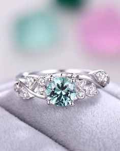 an aqua colored diamond ring on top of a cushioned surface with diamonds around it