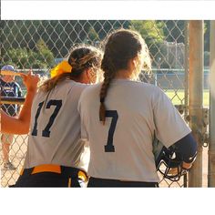 two softball players standing next to each other on a field with their backs turned towards the camera