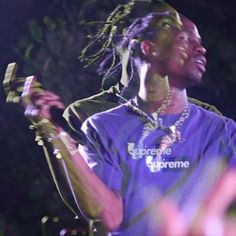 a man with dreadlocks standing in front of a microphone and wearing a purple shirt