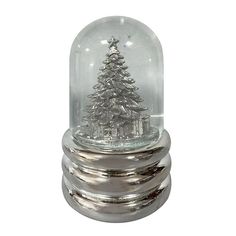 a snow globe with a christmas tree in it on top of three silver plates and a white background