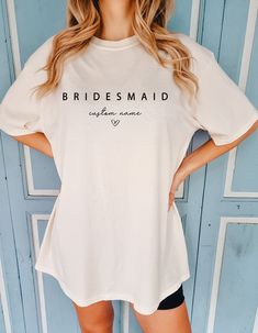 a woman standing in front of a blue door wearing a white t - shirt that says bridesmaid