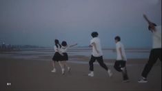 four people are walking on the beach in front of the ocean and one person is holding his arms up