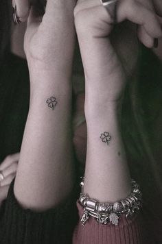 two women with matching tattoos on their arms and wristbands, both holding cell phones