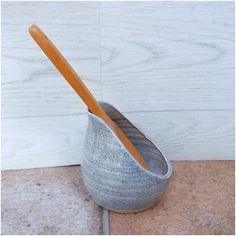 a silver vase with a wooden spoon in it on a tile floor next to a white wall