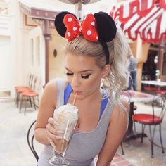 a woman in grey tank top drinking milkshake with minnie mouse ears on her head