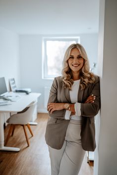 a woman standing in an office with her arms crossed and looking at the camera smiling