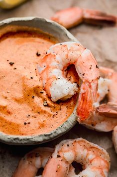 a bowl filled with sauce and shrimp on top of a table next to lemon wedges