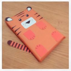 an orange phone case with a tiger design on the front and side, sitting on top of a wooden table