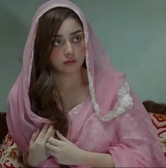 a young woman in a pink dress is sitting on a bed and looking at the camera