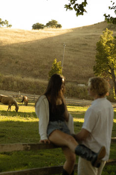 a man and woman standing next to each other on a lush green field with horses in the background