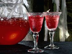 two glasses filled with red liquid sitting on top of a table next to a pitcher