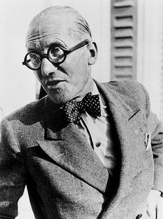 an old man with glasses and a bow tie standing in front of a window wearing a suit