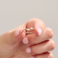 a woman's hand with pink manicured nails holding a gold ring and diamond band