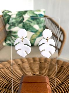 a pair of white earrings sitting on top of a wooden table next to a wicker chair