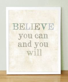 a white framed print with the words believe you can and you will on it sitting on a wooden table