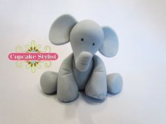 a blue stuffed elephant sitting on top of a white table next to a cupcake stylist logo