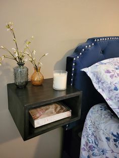 a night stand with a book, candle and flowers on it