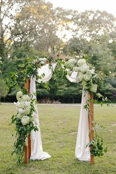 an outdoor wedding ceremony setup with white flowers and greenery on the arch, along with draping