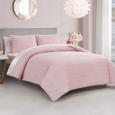 a bed with pink comforter and pillows in a room next to a mirror on the wall