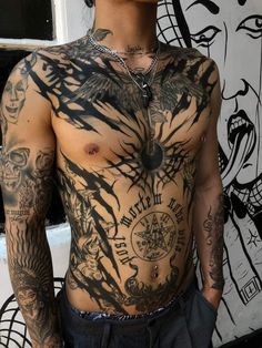 a man with tattoos on his chest standing in front of a wall covered in graffiti